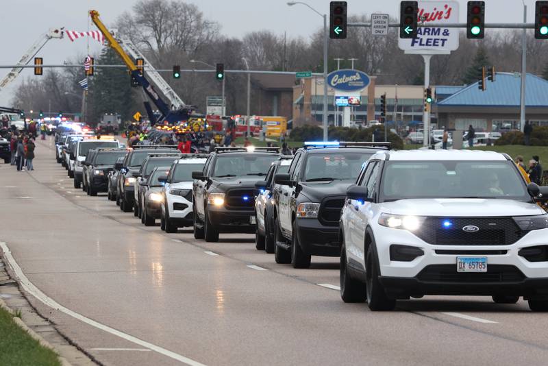 The processional honoring DeKalb County Sheriff’s Deputy Christina Musil travels through people lining the route Monday, April 1, 2024, on DeKalb Avenue in Sycamore. Musil, 35, was killed Thursday while on duty after a truck rear-ended her police vehicle in Waterman.