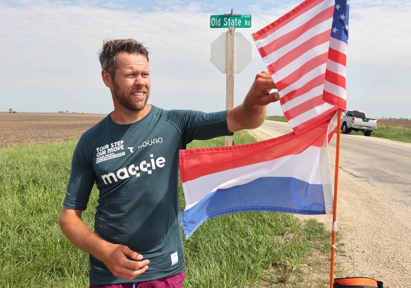 Tom Boerman, from the Netherlands, takes a break from walking Tuesday, May 24, 2022, at the intersection of Old State and Ault Roads near Kirkland to fix his American and Netherlands flags and to have lunch. Boerman, who stopped for the night at a home in DeKalb, is on a quest to walk around the world while raising money for schools in Nepal that were hit hard by the 2015 earthquake in the region.
