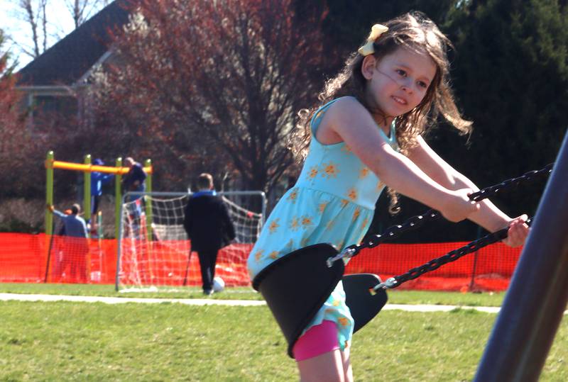 Clarke Kjellman, 5, of Cary swings at an older playground as her father Andrew and many volunteers and friends of Three Oaks Elementary School constructed a new playground at the Cary school on Saturday. Children of volunteers were supervised at the older playground by Three Oaks Principal Kyle Block.