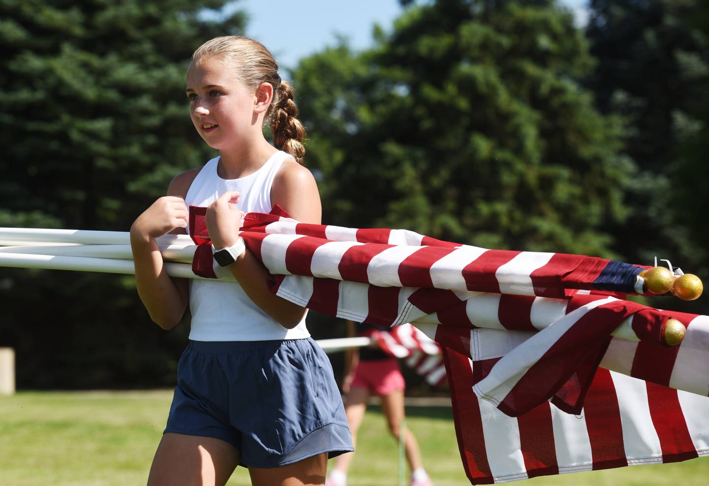 Hannah Lichtenberg, 10, of Wheaton carries flags during setup for the Wheaton Field of Honor at Seven Gables Park on Saturday, June 28, 2025.