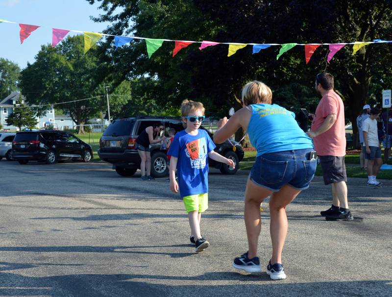 Shauna Zettle holds out a gold medal to RJ Shenberger, 6, as he crosses the finish line of the Cabbage Patch Kids Fun Run on Friday, Aug. 2, 2024, during Forreston Sauerkraut Days.