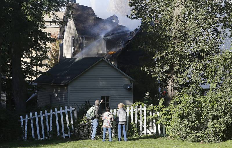 People watch as firefighters battle a house fire in the 300 block of Lincoln Avenue in Woodstock Monday, Oct. 9, 2023, after an explosion following suspected gas leak in the area.