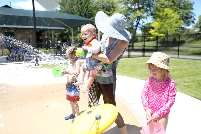 Heather McKeown dips 10-month-old Harlan into the water as Holden, 6, and Hadley, 4, play close-by at the Downers Grove Park District’s Adventure Falls Sprayground at McCollum Park on Friday, June 14, 2024.