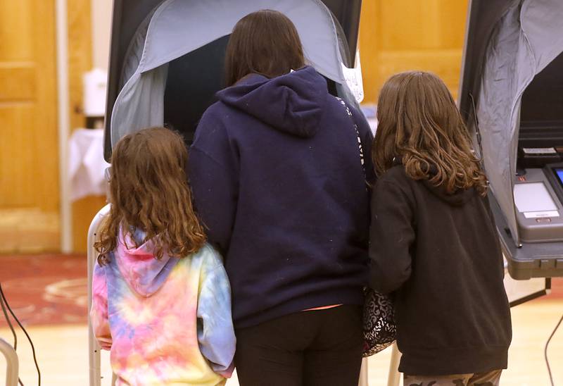 Alexa, Hoving, 7, of Hampshire, (left) and her sister, Julia, 11, (right) watch as their mother, Katie, casts her ballot Tuesday, April 4, 2023, in the 2023 consolidated election at Del Webb Sun City’s Prairie Lodge in Huntley.