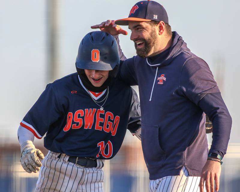 Oswego's TJ Harazin (10) is greeted at first after hitting a single during baseball game between Plainfield South at Oswego on Monday, April 14, 2025 in Oswego.