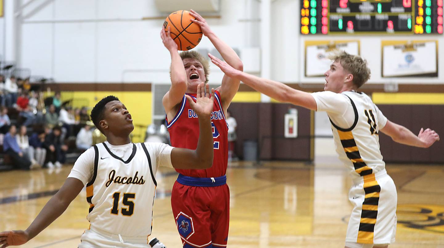 Dundee-Crown's Shane Demarsh shoots the ball between the defense of Jacobs' Chris Williams (left) and Carson Goehring (right) during a Fox Valley Conference boys basketball game on Tuesday, February. 3, 2026, at Jacobs High School in Algonquin.
