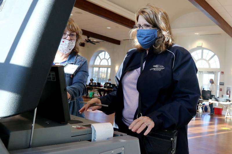 Election judge Jan Baier, left, helps Phyllis Moister of Lakewood with depositing her completed ballot inside the collection machine at Main Beach on Tuesday, Nov. 3, 2020 in Crystal Lake.