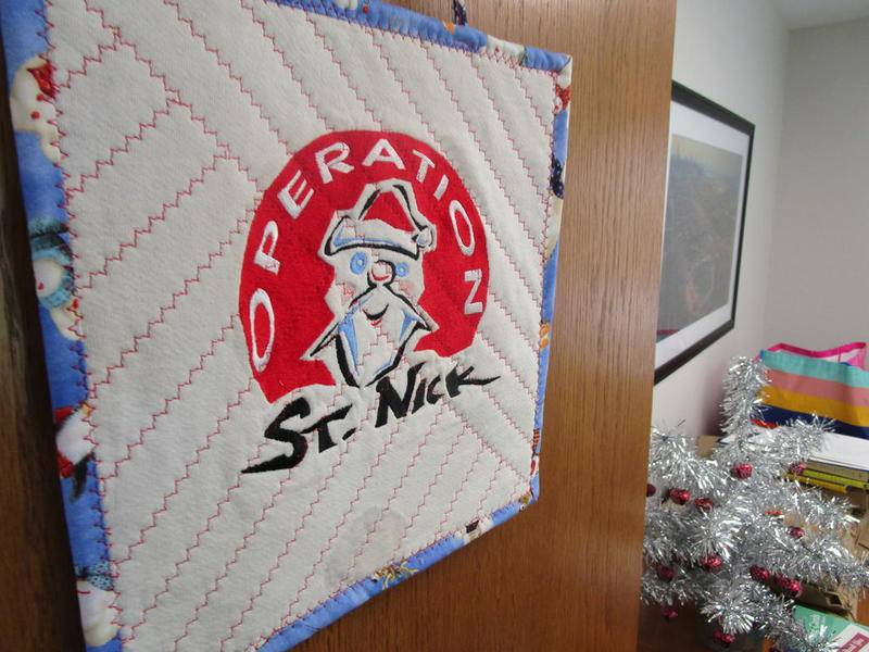 A knitted logo for Operation St. Nick hangs on the office door of Joe Schmidt. This is the 9th year Christmas in July has donated to Grundy veteran families.