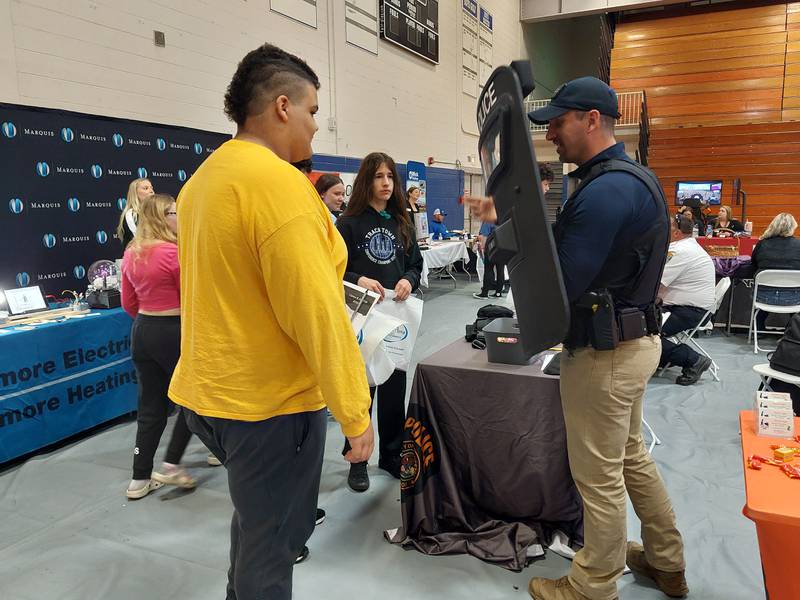 Princeton School Resource Officer Adam Gutshall demonstrates police gear Friday, April 19, 2024, to Princeton Logan eighth grader TJ Kruse-Carter at the Career, Job and Volunteer Fair at Princeton High School.