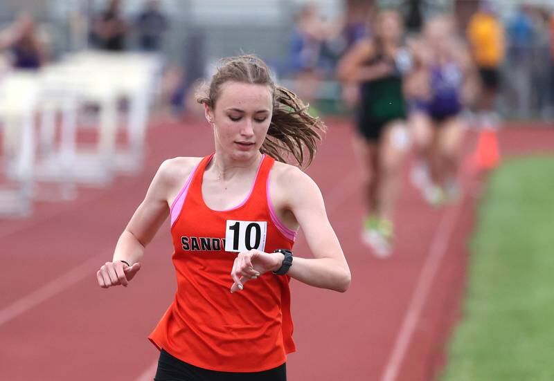 Sandwich’s Sundara Weber checks her watch as she comfortably leads the 3200 meters Wednesday, May 8, 2024, during the girls track Class 2A sectional at Rochelle High School.