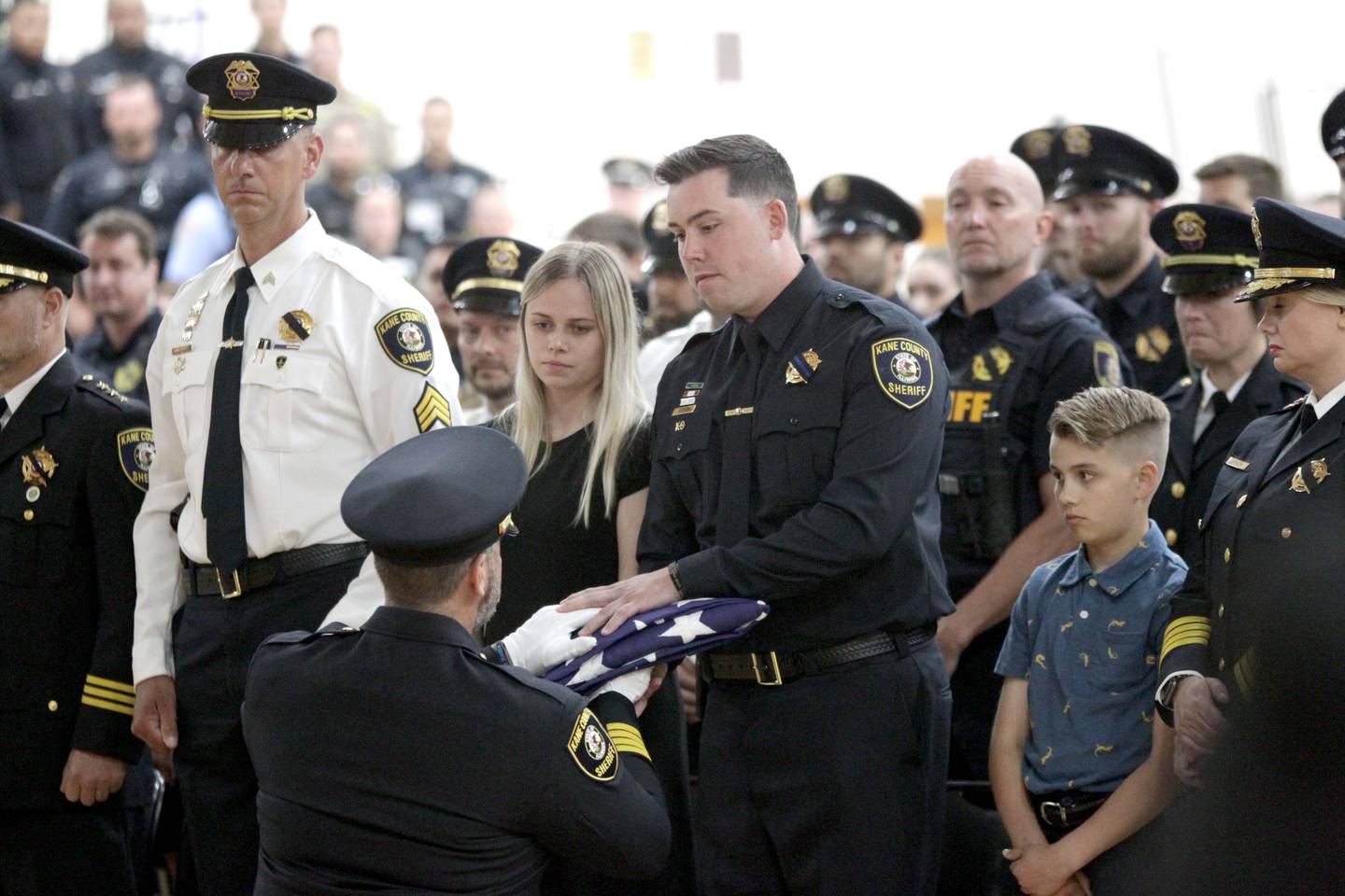 Kane County Sheriff Ron Hain (kneeling) presents an American flag to Kane County Deputy Luke Weston and his wife, Rachel, during a funeral in honor of Kane County Sheriff K9 Hudson, who lost his life in the line of duty last month, on Thursday, June 1, 2023 at Kaneland Harter Middle School in Sugar Grove. Deputy Weston was Hudson’s handler.