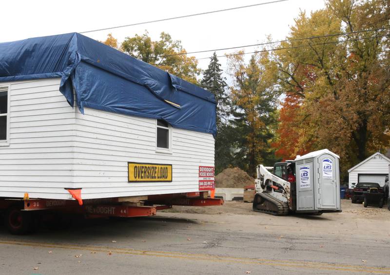 A potable toilet is moved to make way for a home as it is backed into place Tuesday, Oct. 22, 2024, at its new location on Pleasant Street in Dekalb. The home was moved from the DeKalb County History Center property in Sycamore by Devooght House Movers and Habitat For Humanity for Heaven Allen and her son who will be living in the home when it is completed.