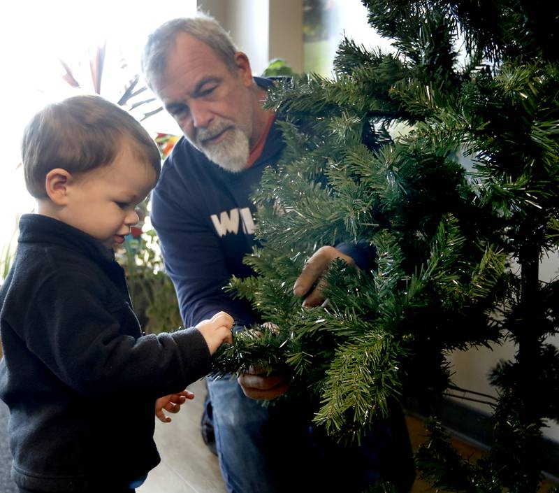 Chase Wohlert, 2, helps Scott Giles fluff the branches on the Reeses Barkery and Pawtique Christmas trees on Thursday, Nov. 16, 2023, as they prepare the tree for the McHenry Chamber of Commerce Festival of Trees at the McHenry Recreation Center. The tree festival runs through Dec. 30, You can vote for your favorite Christmas tree by leaving canned food or toiletries under the tree you like best during normal business hours. All donations go to Veteran’s Path to Hope.