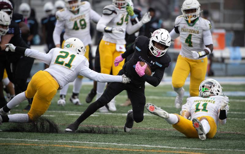 Kankakee's Ezekiel Sherrod, center, carries the ball on a play as Providence Catholic's Anthony Laquinta, left, and Declan Dircks, right, attempt to tackle in a Class 5A playoff on Saturday, November 8, 2025.