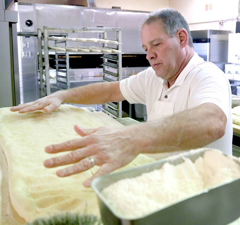 Ken Elleson, owner of Elleson's Bakery, flattens the dough before it is sliced up for paczkis Monday, Feb. 28, 2022, in the kitchen of the bakery in Sycamore. Elleson and members of his family will be working all night making the paczkis from scratch to be ready at 5 a.m. tomorrow for Fat Tuesday.