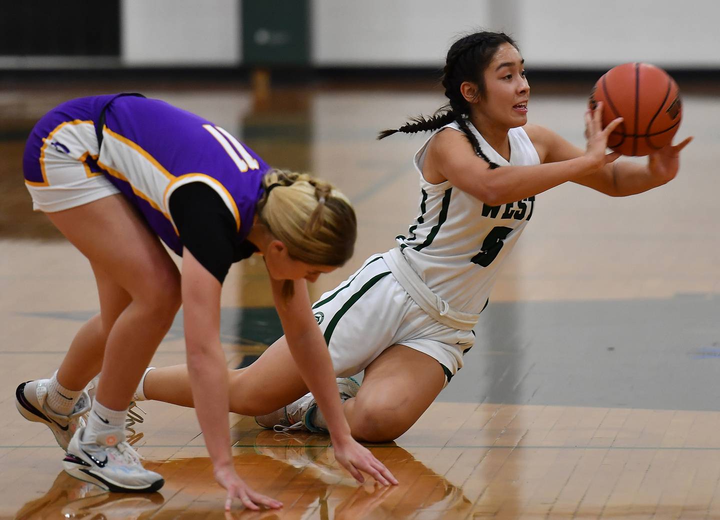 Glenbard West's Lauren Escalante passes from her knees after grabbing a loose ball away from Downers Grove North's Abby Gross (11) during a game on Dec. 5, 2023 at Glenbard West High School in Glen Ellyn.