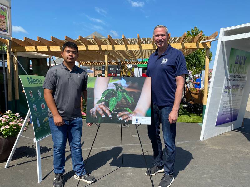 Plano teen Adan Silva, left, stands next to his winning photo, "The Beauty in Planting," at the Illinois State Fair. Standing next to him is Illinois State Treasurer Michael Frerichs, right.