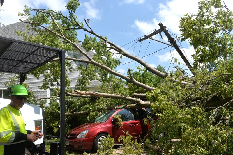 An Asplund tree trimmer looks at  a large tree that was blown over in Friday's  early morning storm at the corner of Van Buren and W. Fourth Street in Dixon. Zachary Taylor's home, pictured here, escaped major damage but the tree crushed his red van. Several ComEd and Asplundh crews were dispatched  to the area to repair damaged electrical lines and poles in an effort to restore power to residents in the area as temperatures climbed into the mid 90s.