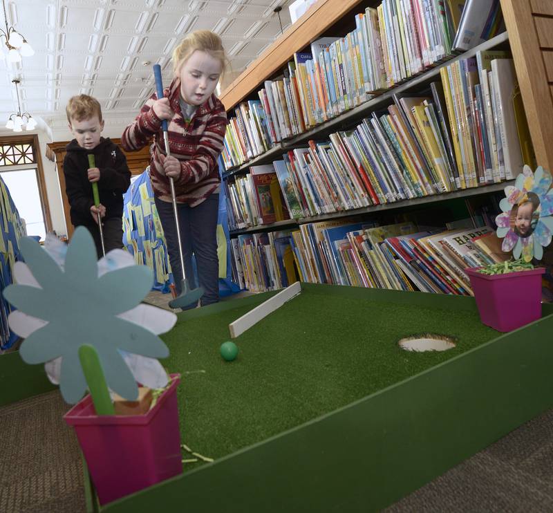 With her brother Jacob inching up to the hole,Allie Coonan tries to sink her putt Saturday during the Carnegie Challenge Mini Golf FUN-Raiser at the Streator Public Library.