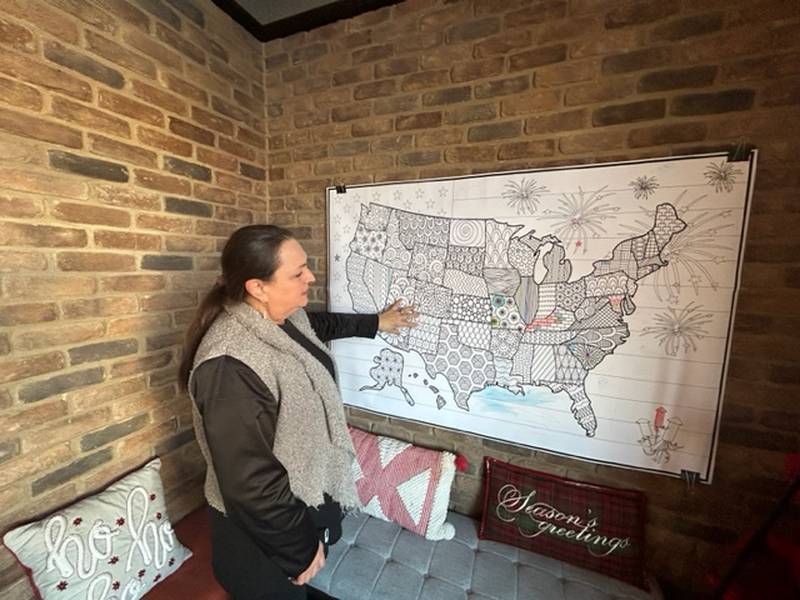 Shelli Eng points to a coloring page hanging on the wall in her business, The Bread Lady at Donnybrook. People who stop by the bakery can color on the page, which will be sold to raise money for charity.