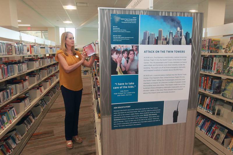 Nami Quaranta, of Lindenhurst, learning & development coordinator, puts away an audiobook close to a 9/11 poster on display to commemorate the 20th Anniversary of 9/11 at the Lake Villa District Library in Lindenhurst. Fourteen 9/11 posters are on display which came from the 9/11 National Memorial & Museum  in New York. (9/7/21)