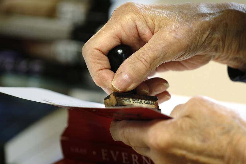 Librarian Dorothy Peterson works on adhering new stickers to the spines of books, stamping them with a "Hebron Public Library" stamp, attaching library loan cards to the inside covers, and finding a home for them on the shelves beside other books available for checkout inside the recently restored Hebron Public Library on Wednesday, April 7, 2021, in Hebron.