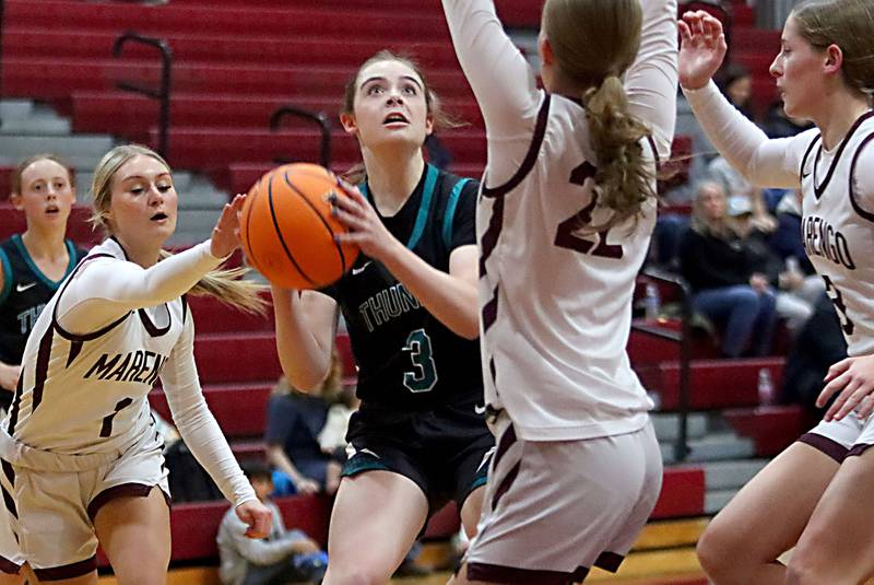 Woodstock North’s Addy Crabill, center, gets past Marengo’s Myah Broughton, left, in varsity girls basketball on Tuesday, Dec. 2, 2025, at Marengo High School in Marengo.
