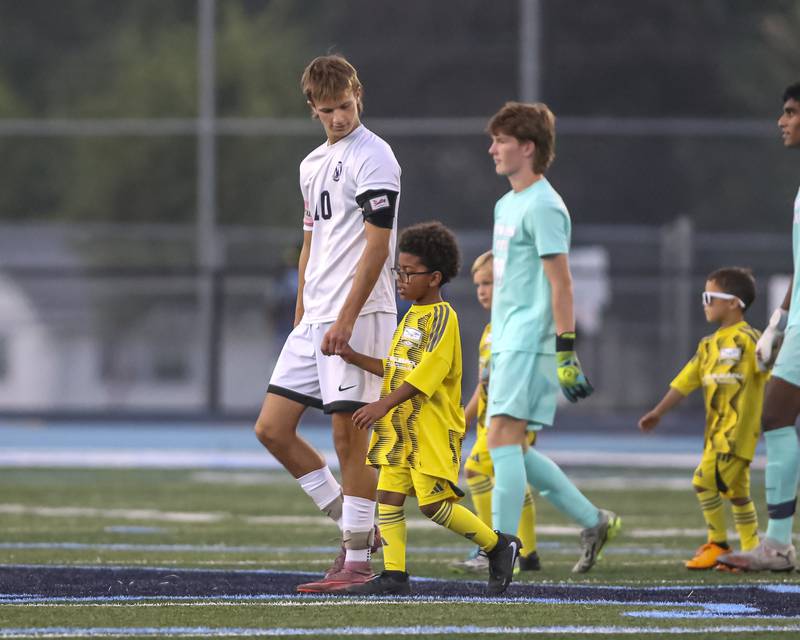 Downers Grove North's Oliver Davies (10) escorts a small soccer player onto the field before pregame introductions before soccer match between Downers Grove North at Downers Grove South. Oct 2, 2025.