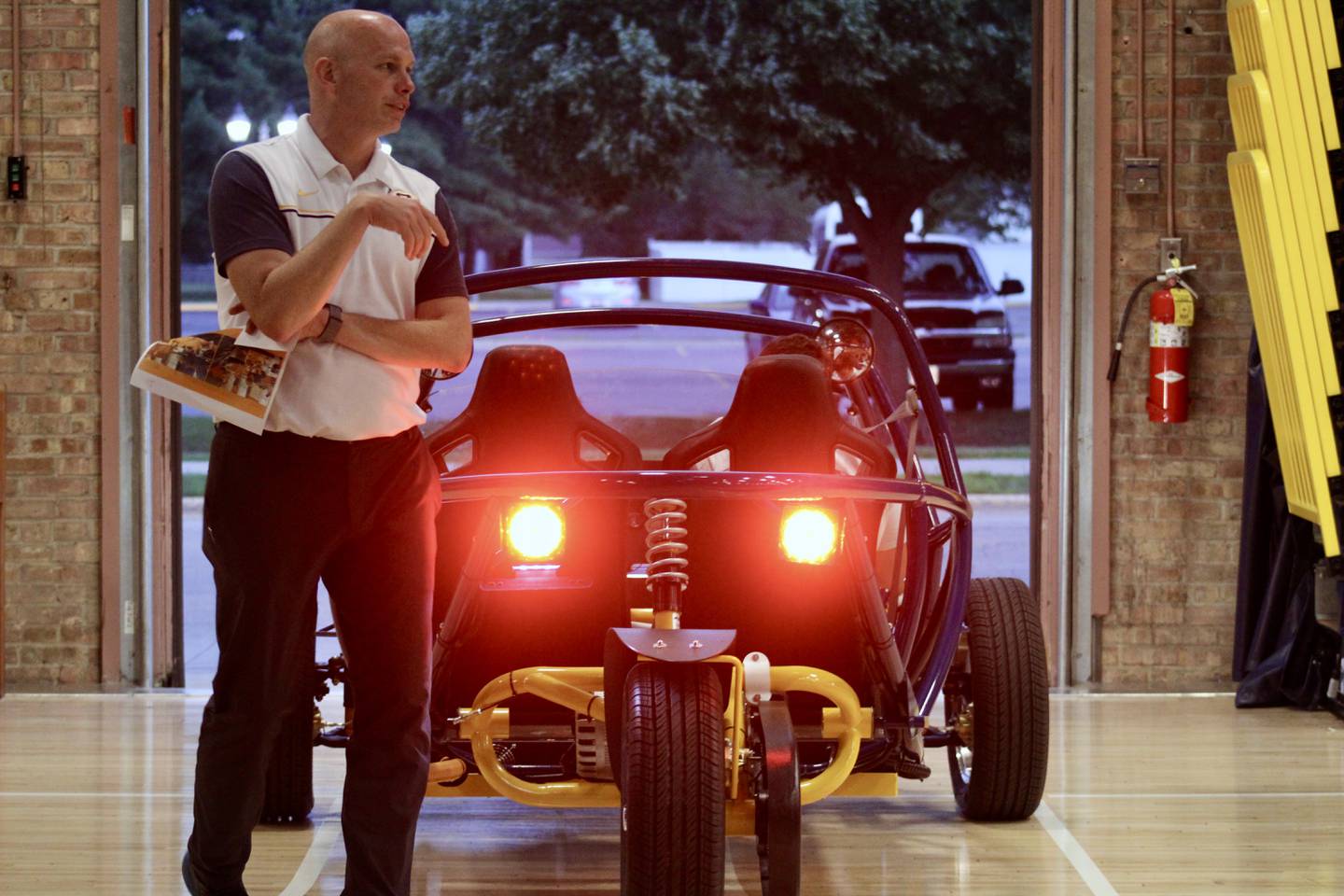 Sterling High School Principal Justin Austin explains aspects of the Switch electric vehicle that physics students assembled, as Paige Geil and Zach Shapiro drive it out of Musgrove Fieldhouse, where it had been staged for a demonstration.