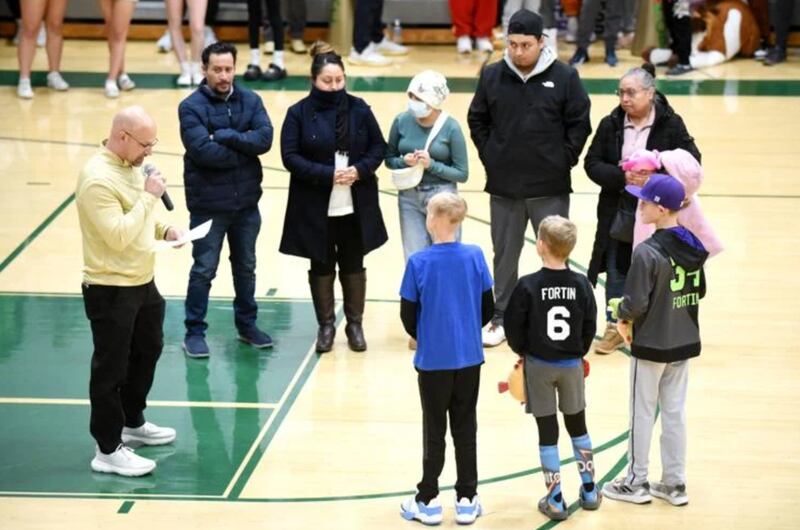 Bishop McNamara boys basketball coach Adrian Provost, left, speaks during a ceremony at the team’s child cancer night game against Manteno. Looking on are the families of Alexandra Ramos, top center, and Carter Fortin, blue shirt, who are both going through cancer battles. They Fightin’ Irish held child cancer night during Tuesday’s home game against Manteno.