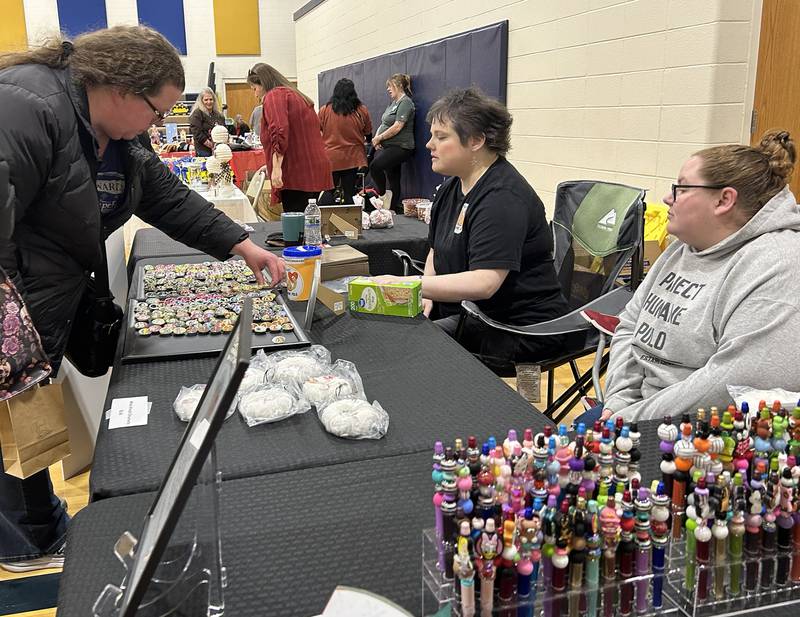 Erica Sexton of Rock Falls chooses an item to purchase at the Project Humane booth at the Polo Christmas Festival's Craft and Vendor Show on Saturday, Dec. 6, 2025. Ashley Rinehart and Jessica Lindsey were manning the booth.