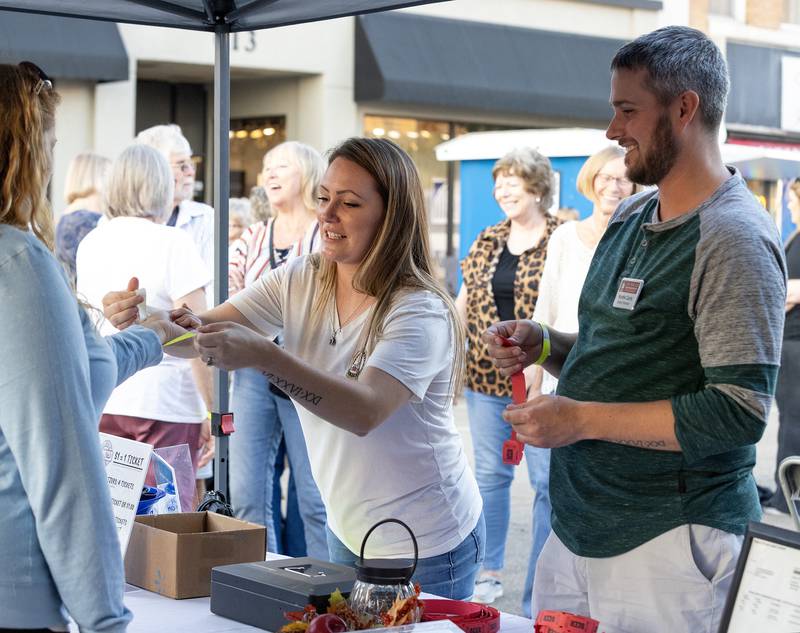 Katie Carls attaches a wristband to a festival goer Saturday evening at the LaSalle Business Association's Jazz'N the Street event while her husband, Kurtis Carls, sells drink tickets.