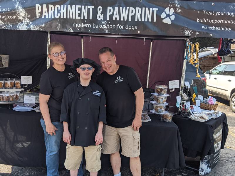 Oswego resident Zachary Pietrowiak, center, bakes wholesome dog treats for his family business,  Parchment & Pawprint, which sells its products at the Oswego Country Market. At left is his mother, Christine Pietrowiak, co-founder of the business, and at right is his father, Russell Pietrowiak.