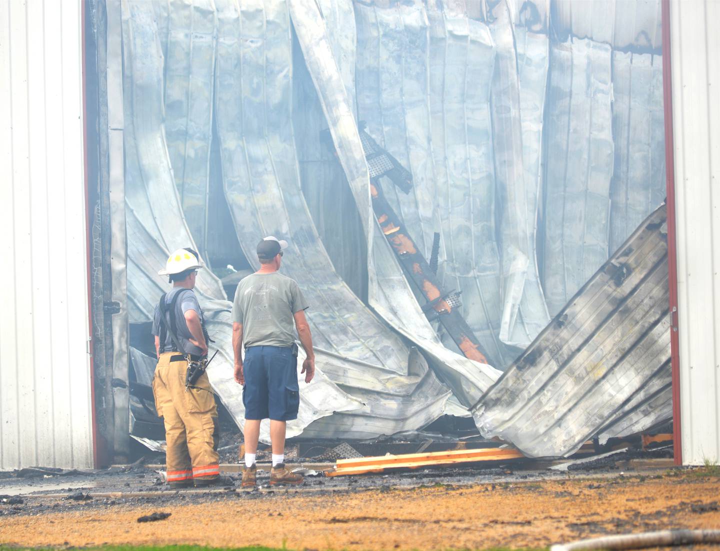 Two firefighters examine the charred remains of a large machine shed that was destroyed by a fire north of Dixon on Friday morning.