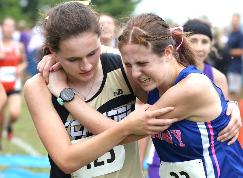 Sycamore's Lily Baker helps injured Aurora Rosary runner Olivia Kunio after they crossed the finish line together in the varsity girls race Tuesday, Aug. 31, 2021 at the Sycamore Cross Country Invitational at Kishwaukee College in Malta.