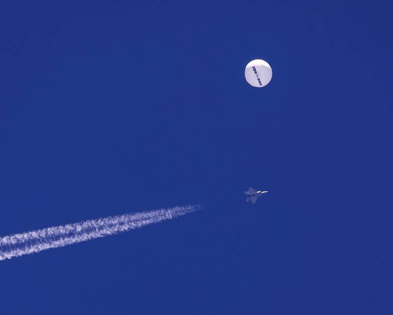 In this photo provided by Chad Fish, a large balloon drifts above the Atlantic Ocean, just off the coast of South Carolina, with a fighter jet and its contrail seen below it, Saturday, Feb. 4, 2023. The balloon was struck by a missile from an F-22 fighter just off Myrtle Beach, fascinating sky-watchers across a populous area known as the Grand Strand for its miles of beaches that draw retirees and vacationers.  (Chad Fish via AP)