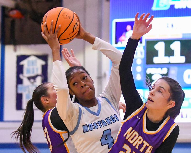 Downers Grove South's Hayven Harden (4) gets a rebound during the game on Saturday Dec. 21, 2024, while being defended by Downers Grove North's Gianna Goodwin, left, and teammate Downers Grove North's Caitlin Sandrige  (25) held at Downers Grove South High School.