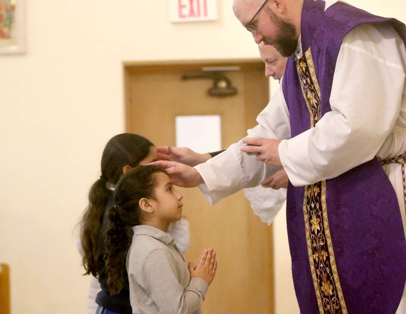 The Very Rev. Father Tom Otto places ashes on the forehead of Nevaeh Pagan, a student at Trinity Catholic Academy during Ash Wednesday Mass on Wednesday, March 5, 2025 at the Queen of the Holy Rosary Church in La Salle.