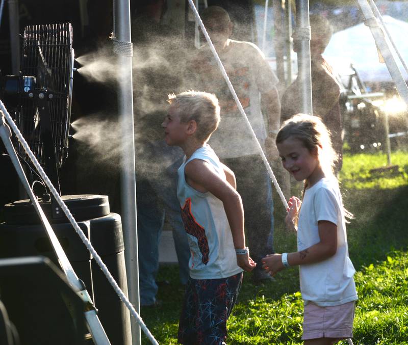 Two kids cool off at a mist fan at the Ogle County Fair on Friday, Aug. 2, 2024.
