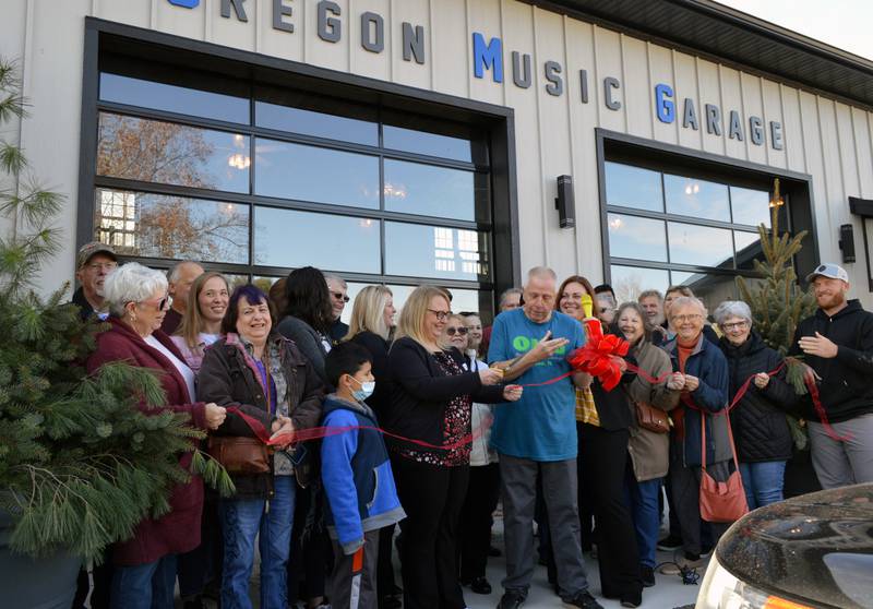 John Lindhorst (center, blue shirt), owner of Ukulele Station America, watches as Christy Eastman, of Union Savings Bank, cuts a ribbon during the Nov. 20 grand opening of his new business, Oregon Music Garage. Lindhorst worked with Union Savings Bank to finance the project.