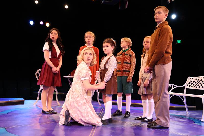 Maria (Cassidy Hamilton, kneeling) holds the hands of Gretl (Ava Doty of Downers Grove). Behind Maria is Brigitta (Aubrey Doty of Downers Grove).