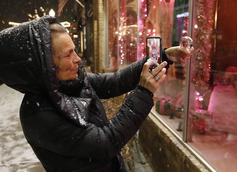 Katja Waehner takes a photograph a stores window with a lens ball during Crystal Lake's Luminary Nights on Thursday, Dec. 19, 2024, in downtown Crystal Lake. The snowy night featured sidewalks lite luminaries, holiday shopping and a visit to the Santa House.
