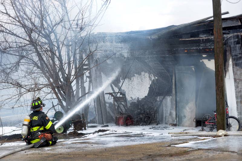 A Mt. Morris firefighter sprays down a garage at 6727 W. Henry Road, southeast of Polo, on Wednesday, March 26, 2025.