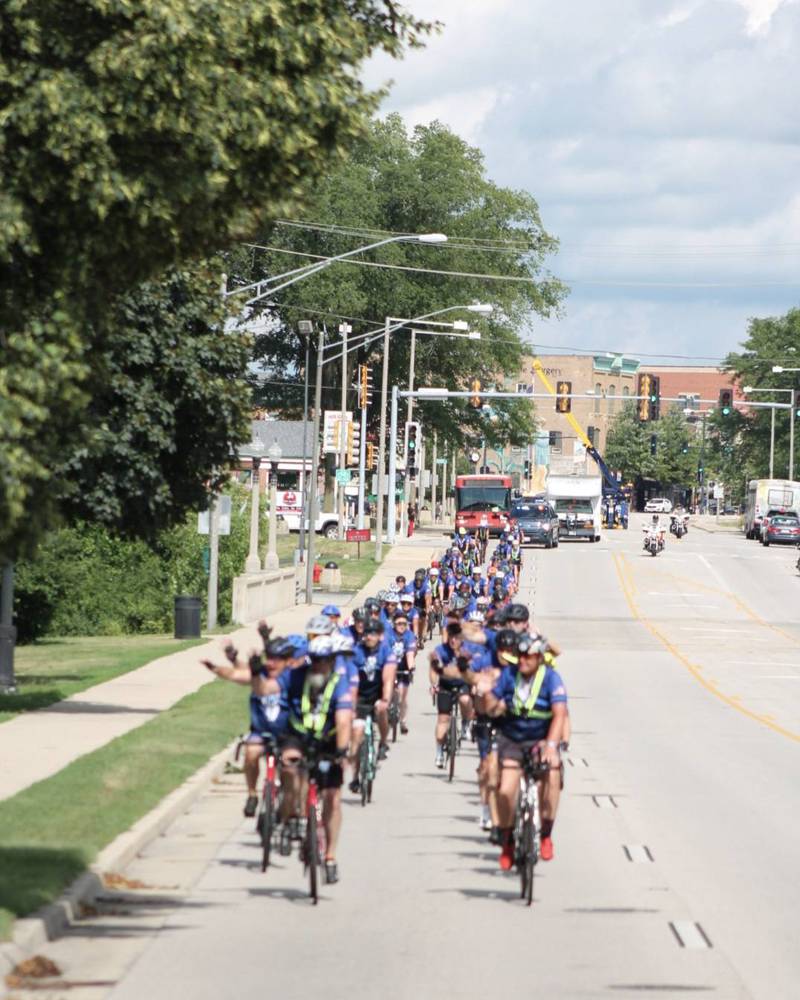Onlookers wave to bicyclists as they make their way through downtown DeKalb along Lincoln Highway (Illinois Route 38) toward Northern Illinois University on Saturday, July 12, 2025. Nearly 100 cyclists biked from Normal to DeKalb for Cycle Across Illinois, a charity campaign to honor fallen police officers and raise funds for their families.