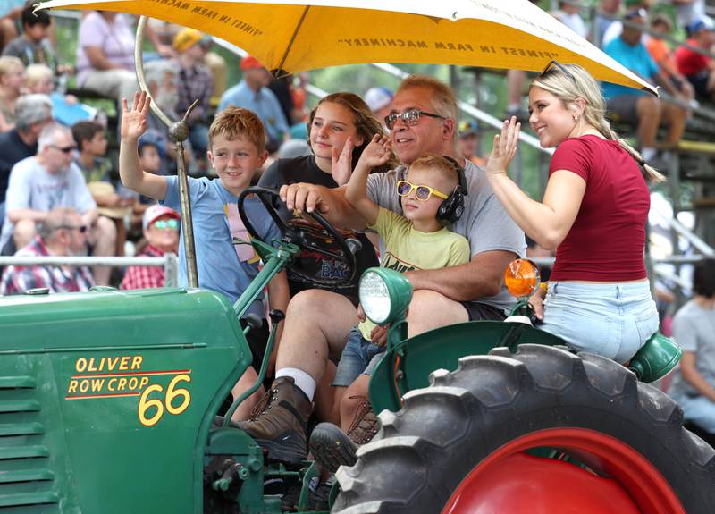 A group waves to attendees as they drive their Oliver Row Crop 66 tractor through the parade Thursday, Aug. 7, 2025, at the 68th annual Sycamore Steam Show and Threshing Bee at Taylor Marshall Farm on Lukens Road in Sycamore.