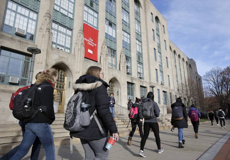 FILE - Students and passers-by walk past an entrance to Boston University College of Arts and Sciences, Nov. 29, 2018, in Boston. As more than 2 million graduating high school students from across the United States finalize their decisions on what college to attend this fall, many are facing jaw-dropping costs — in some cases, as much as $95,000.