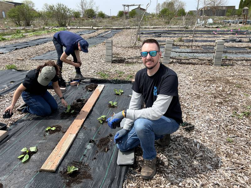 Adam Roach pauses for a picture as his IDEAL Industries coworkers, Maribel Silva and Sam Jaros continue to plant crops as part of a volunteer opportunity their employer setup through DeKalb County Community Gardens for Earth Day on April 22, 2024.