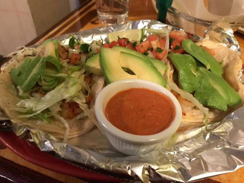 The shrimp tacos dish at Los Panchos includes three corn tortillas topped with shrimp, pico de gallo, lettuce, avocado, onion and tomato. It comes with a side of hot sauce and a plate of Spanish rice.