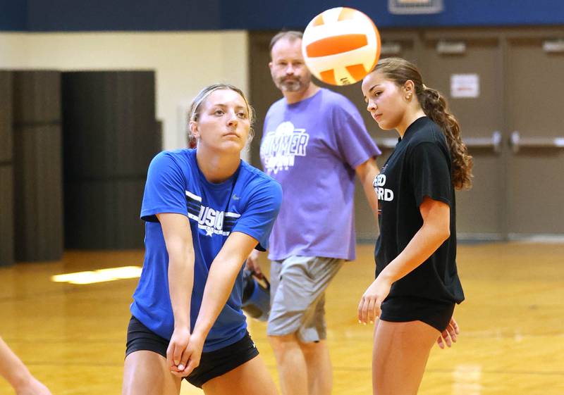 Genoa-Kingston’s Alayna Pierce bumps the ball as head coach Keith Foster and teammate Alivia Keegan look on during a drill at practice Thursday, Aug. 10, 2023, at the school in Genoa.