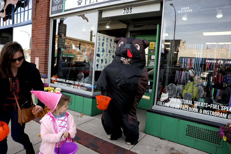 Kiandra Powell, dressed as a dog, offers candy to costumed children outside the Pug and Hound Pet Apothecary during a trick-or-treating event at Geneva businesses on Thursday, Oct. 27, 2022.